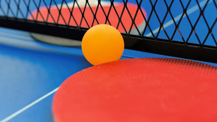 Auschnitt einer Tischtennisplatte mit Netz, Schläger und Ball