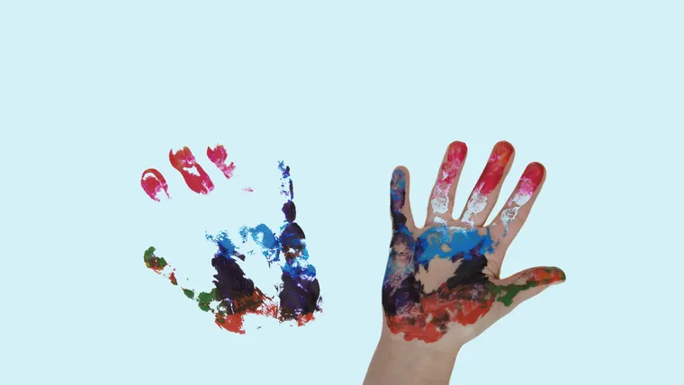 Bunt bemalte Kinderhand, daneben der schemenhafte Abdruck