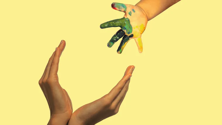 Kleine bunte Kinderhand streckt sich zwei geöffneten Erwachsenenhänden entgegen.