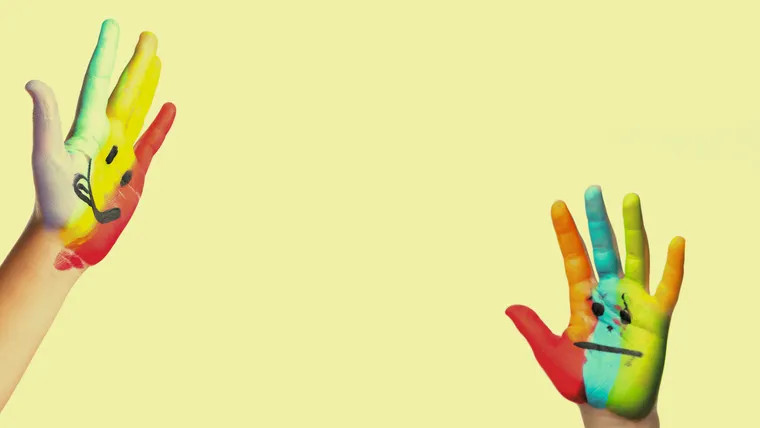 Zwei bunt bemalte Kinderhände, eines mit fröhlichem, das andere mit unglücklichem Smiley