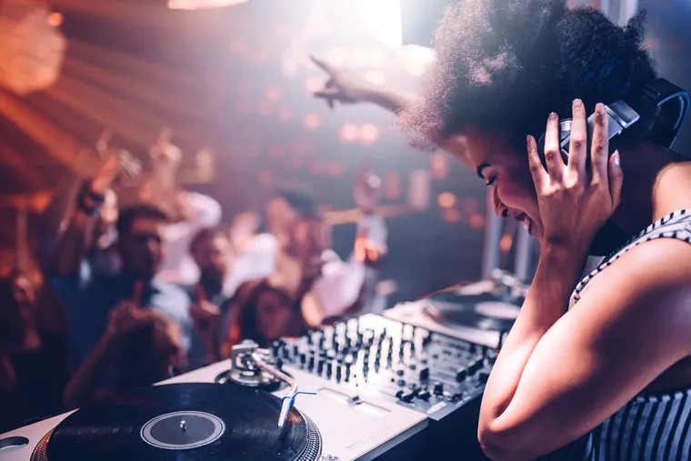Junge DJ am Mischpult, davor tanzende Menschen